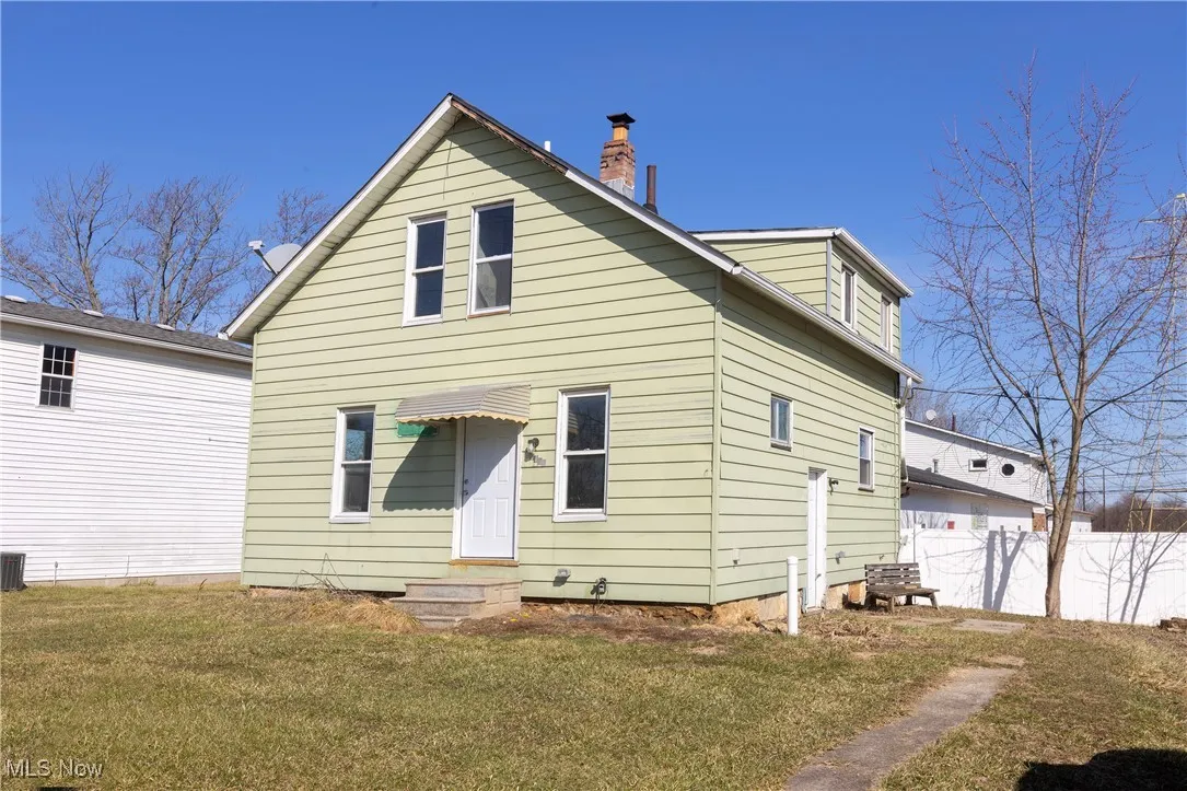 Rear view of property featuring a yard, central AC, a chimney, and fence