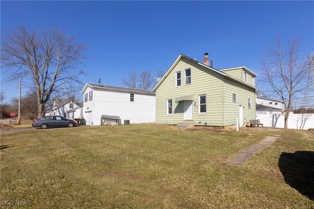 Rear view of property featuring entry steps, a chimney, a yard, and fence