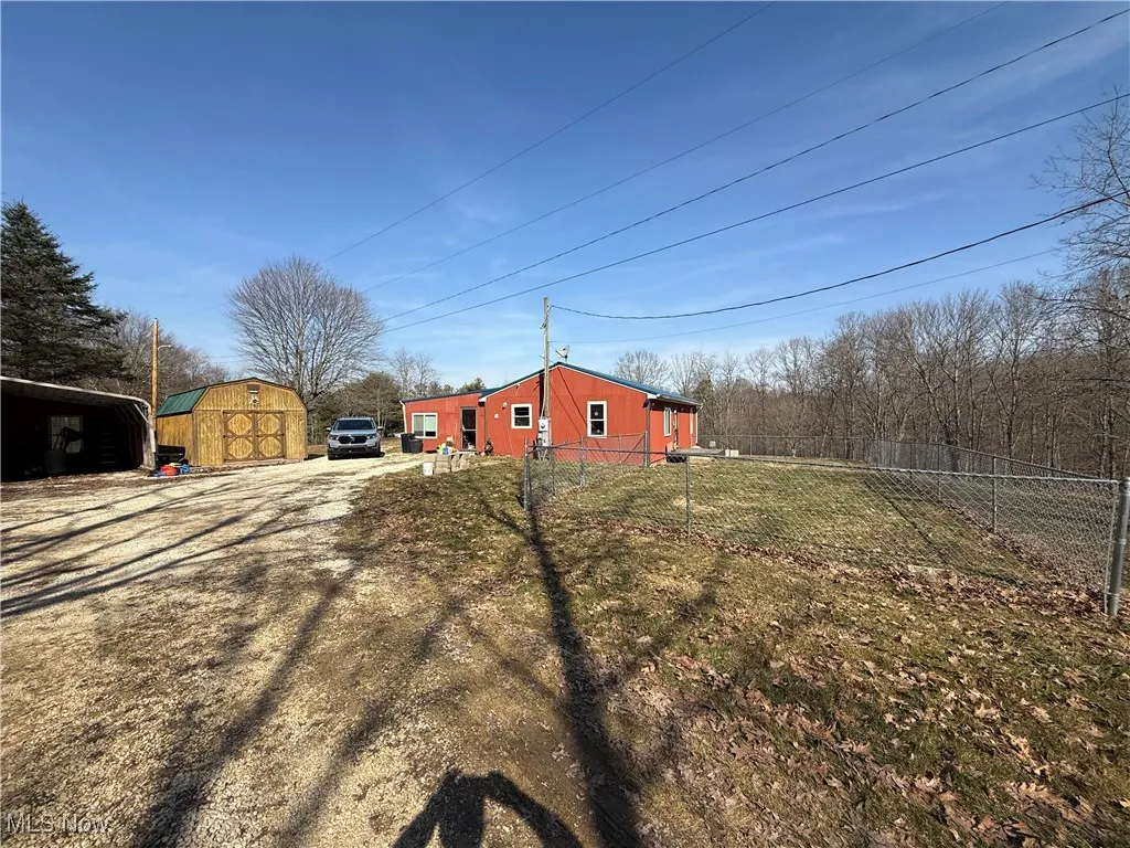 View of yard with a storage unit, an outbuilding, dirt driveway, and fence