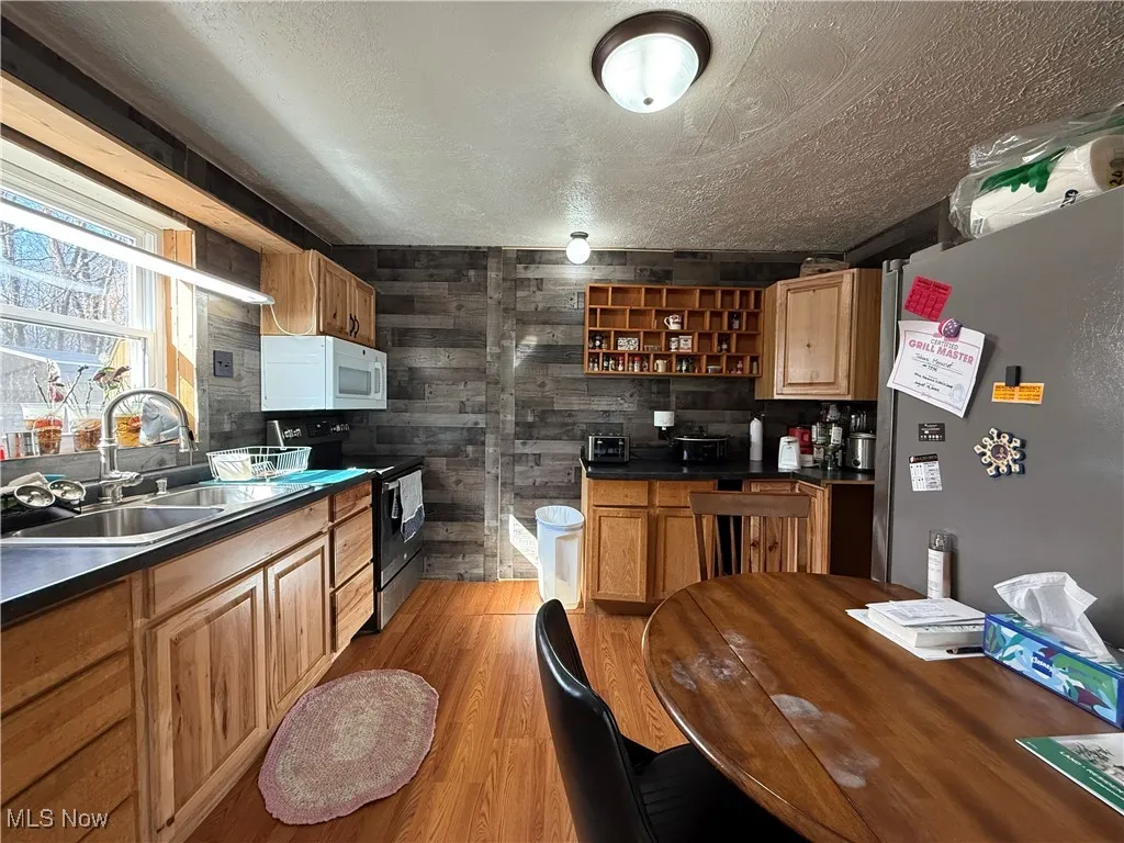 Kitchen with dark countertops, a sink, black range with electric stovetop, light wood-style floors, and open shelves