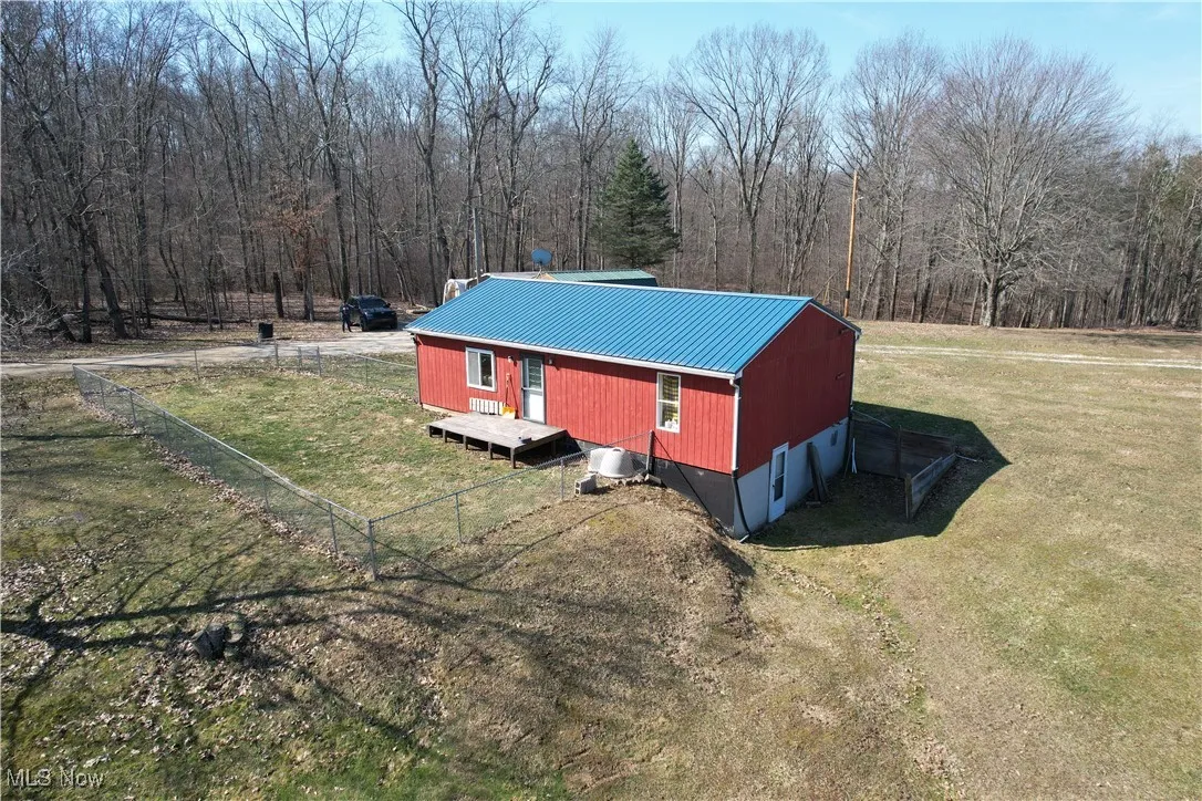 View of property exterior featuring a lawn, a view of trees, metal roof, and fence