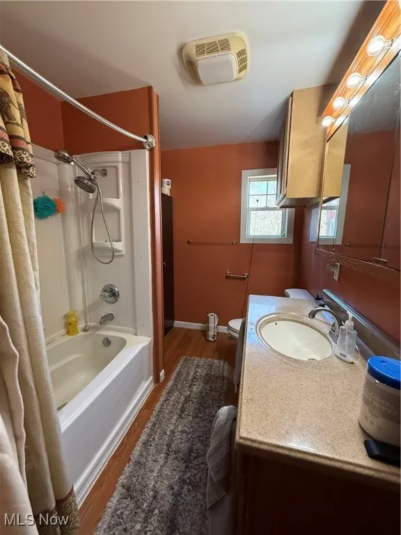 Full bath with baseboards, toilet, shower / bath combo, wood finished floors, and vanity