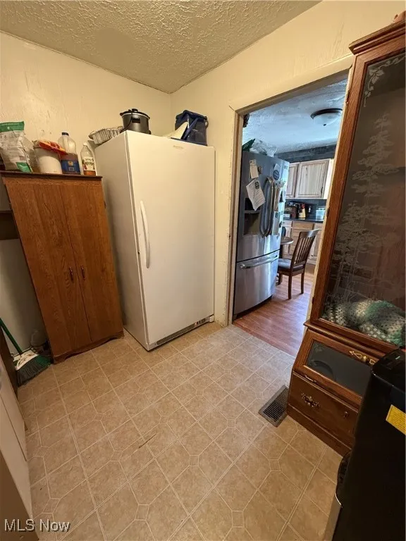 Kitchen featuring visible vents, light floors, freestanding refrigerator, refrigerator, and a textured ceiling