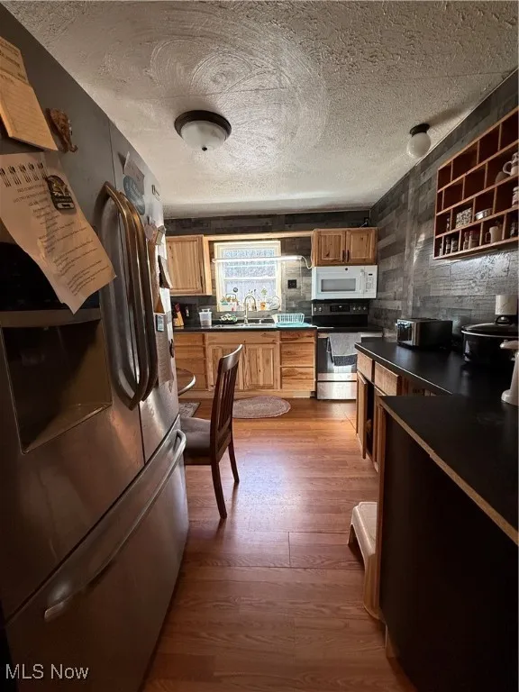 Kitchen with dark countertops, a textured ceiling, dark wood finished floors, fridge, and range