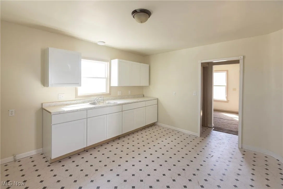 Kitchen with white cabinetry, light countertops, baseboards, and a sink
