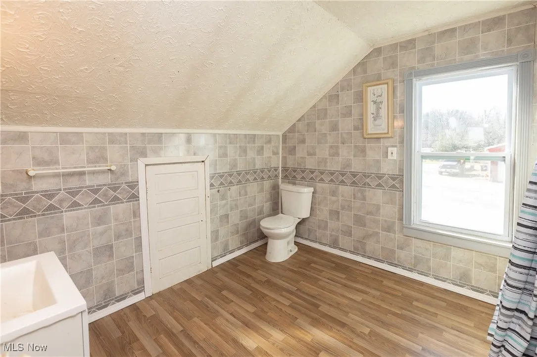 Full bathroom with tile walls, wood finished floors, and a healthy amount of sunlight