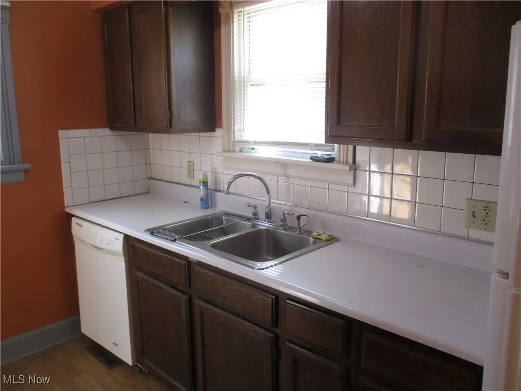Kitchen with a sink, backsplash, white appliances, light countertops, and baseboards