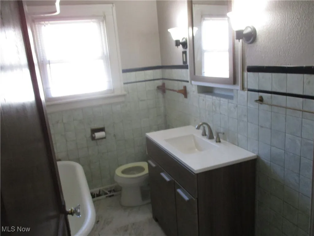 Full bathroom with tile walls, a healthy amount of sunlight, toilet, and vanity