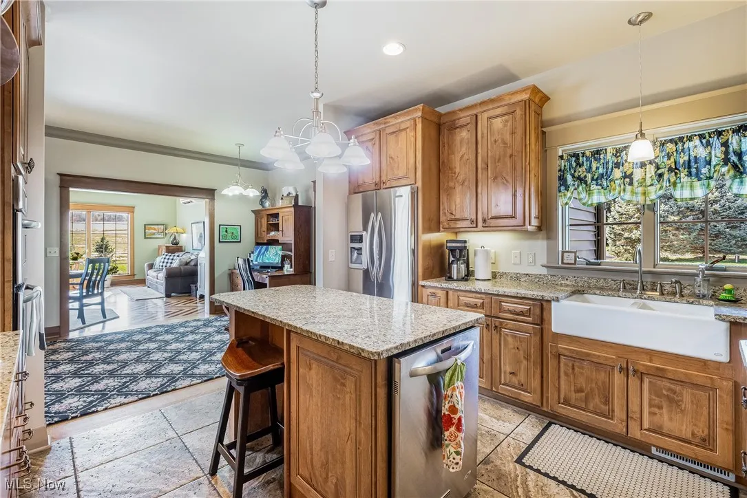Kitchen with a kitchen island, light granite counters, hanging light fixtures, stainless steel appliances, and a farm sink