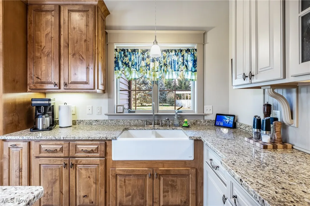 Kitchen featuring light granite counters,  hanging pendant  light fixtures, w cabinetry, and a farm sink
