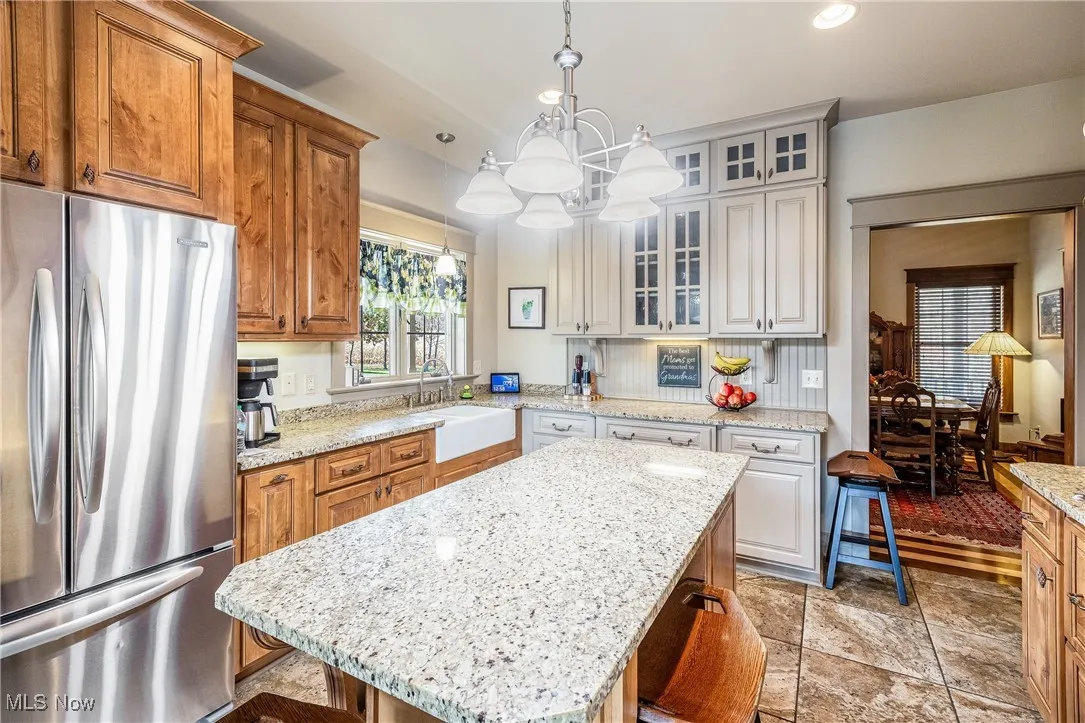 Kitchen featuring a center island, glass insert cabinets, freestanding refrigerator, a sink, and a kitchen bar