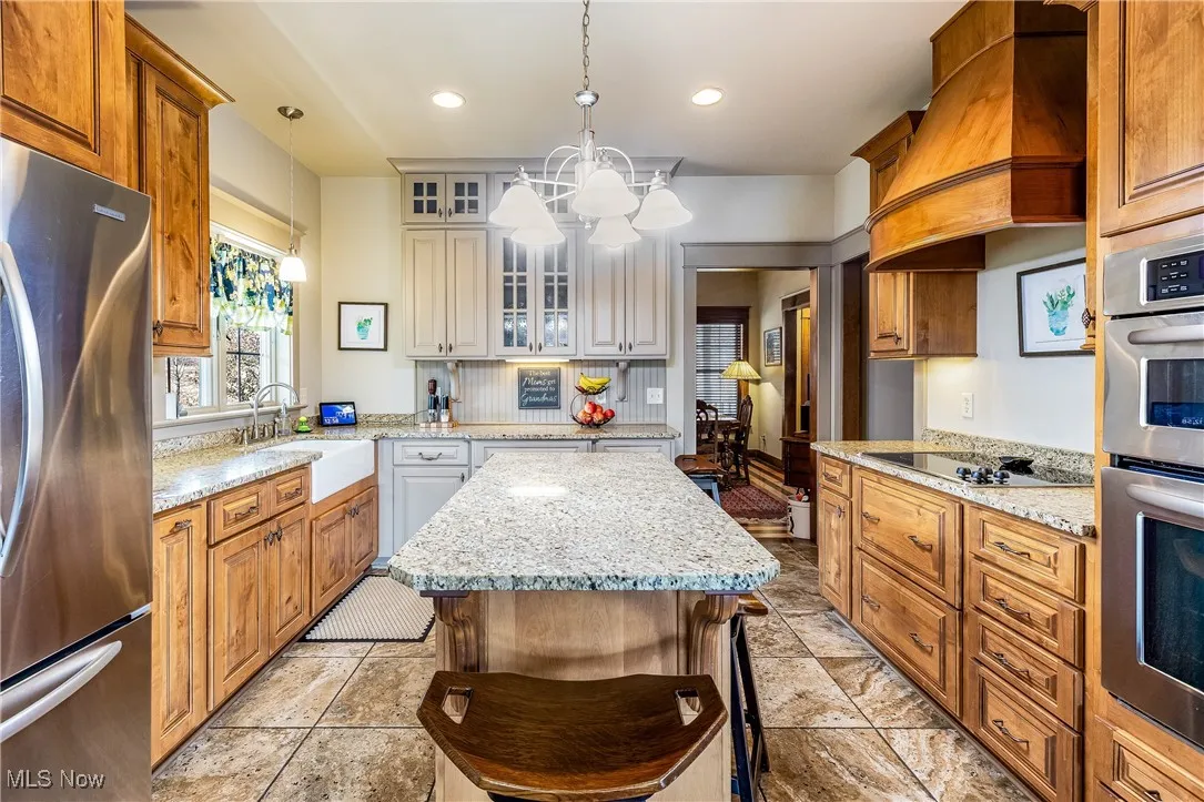 Kitchen with stainless steel appliances, premium range hood, a sink, glass insert cabinets, and pendant lighting