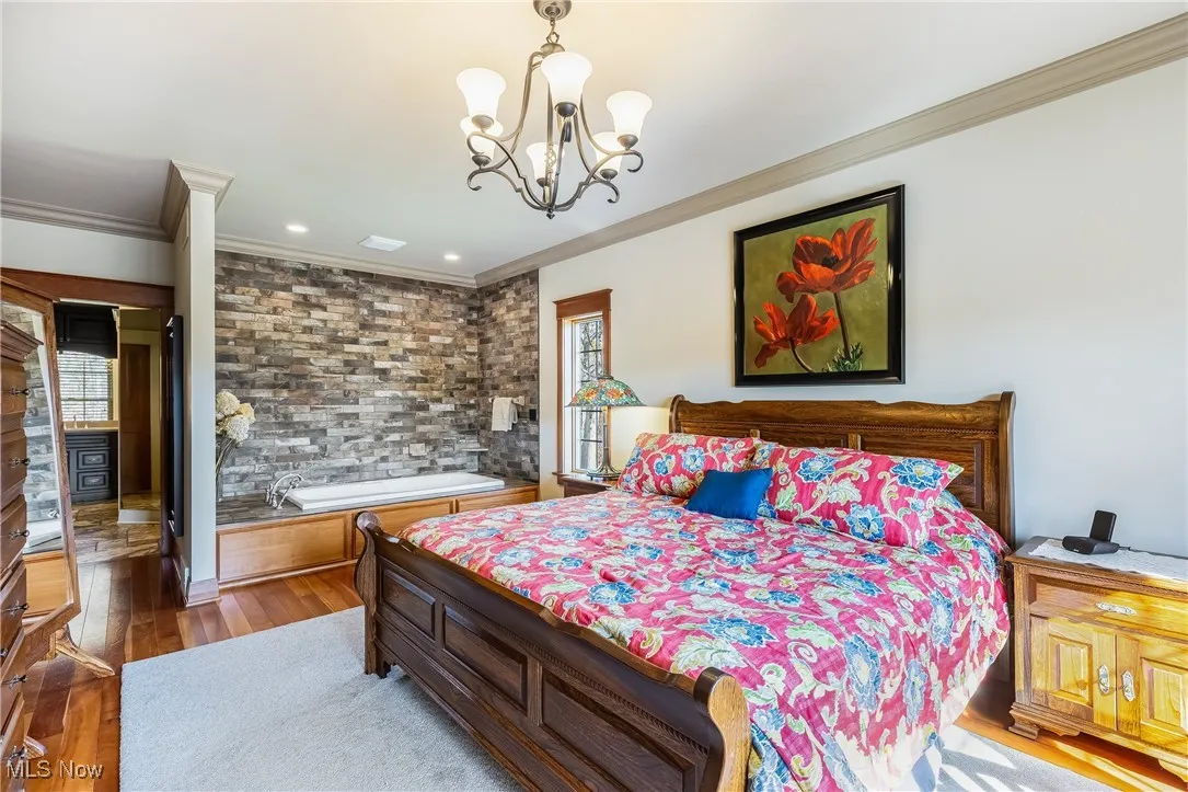 Bedroom featuring an inviting chandelier, ornamental molding, and whirlpool spa tub stone veneer wall surround