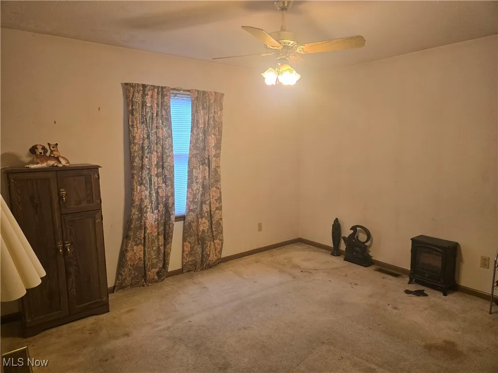 Spare room featuring a ceiling fan, light colored carpet, visible vents, and a wood stove