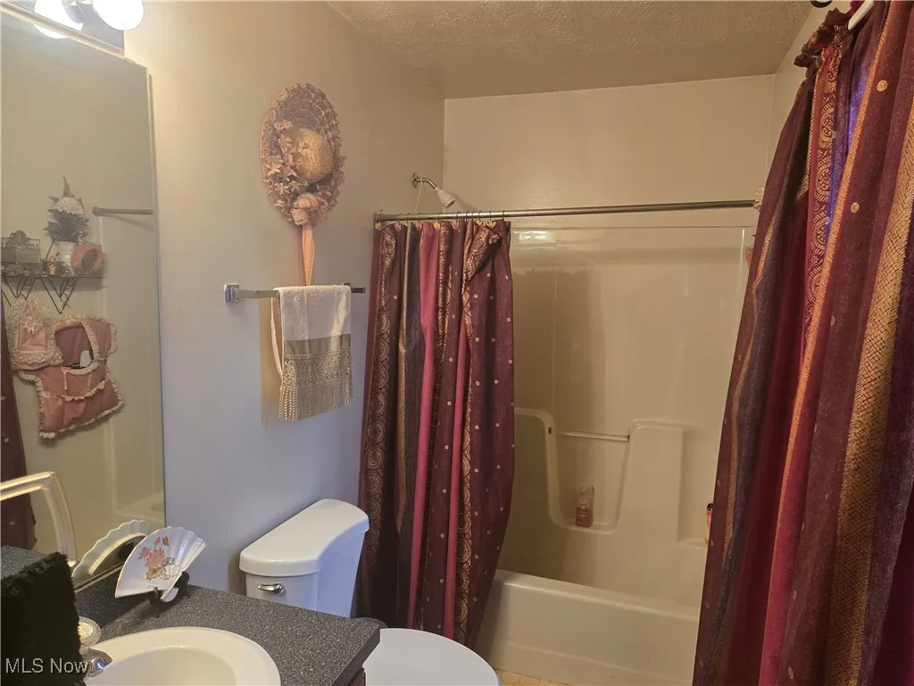 Bathroom with shower / bath combo with shower curtain, a textured ceiling, vanity, and toilet