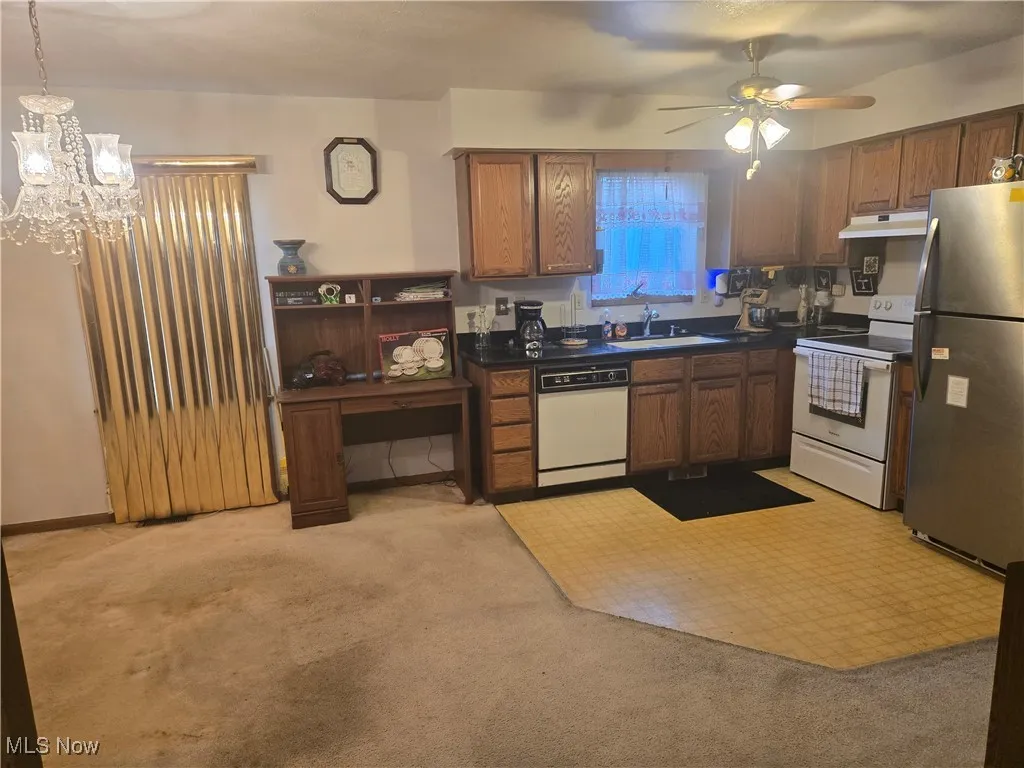 Kitchen with white appliances, a sink, under cabinet range hood, dark countertops, and light colored carpet