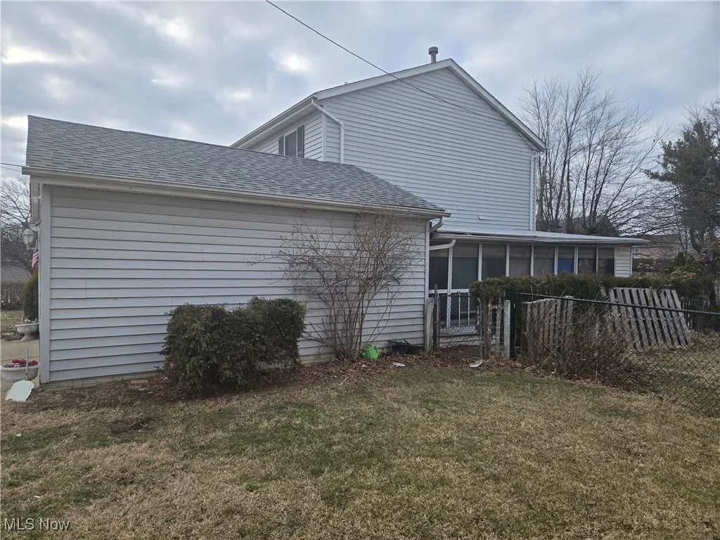 View of side of home featuring a lawn, fence, roof with shingles, and a sunroom