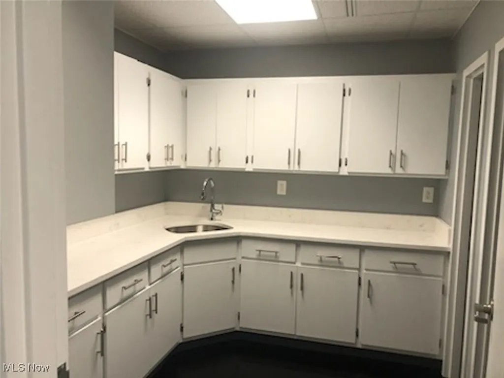 Kitchen featuring a drop ceiling, white cabinets, light countertops, and a sink