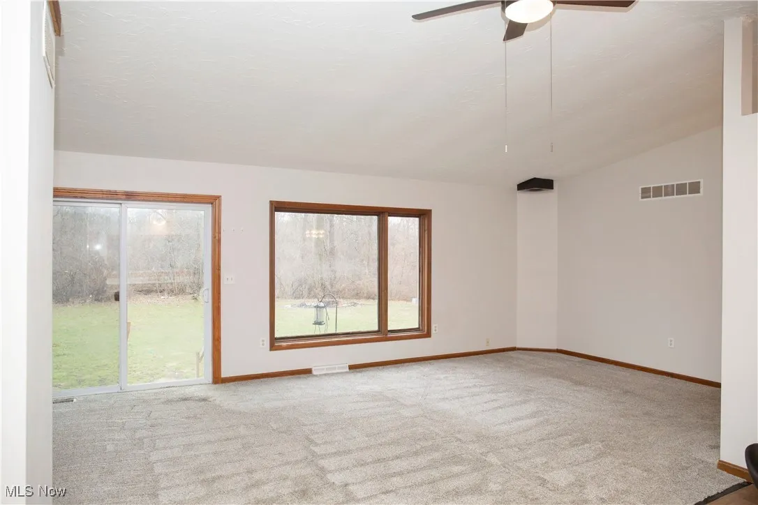 Carpeted empty room with visible vents, plenty of natural light, and ceiling fan