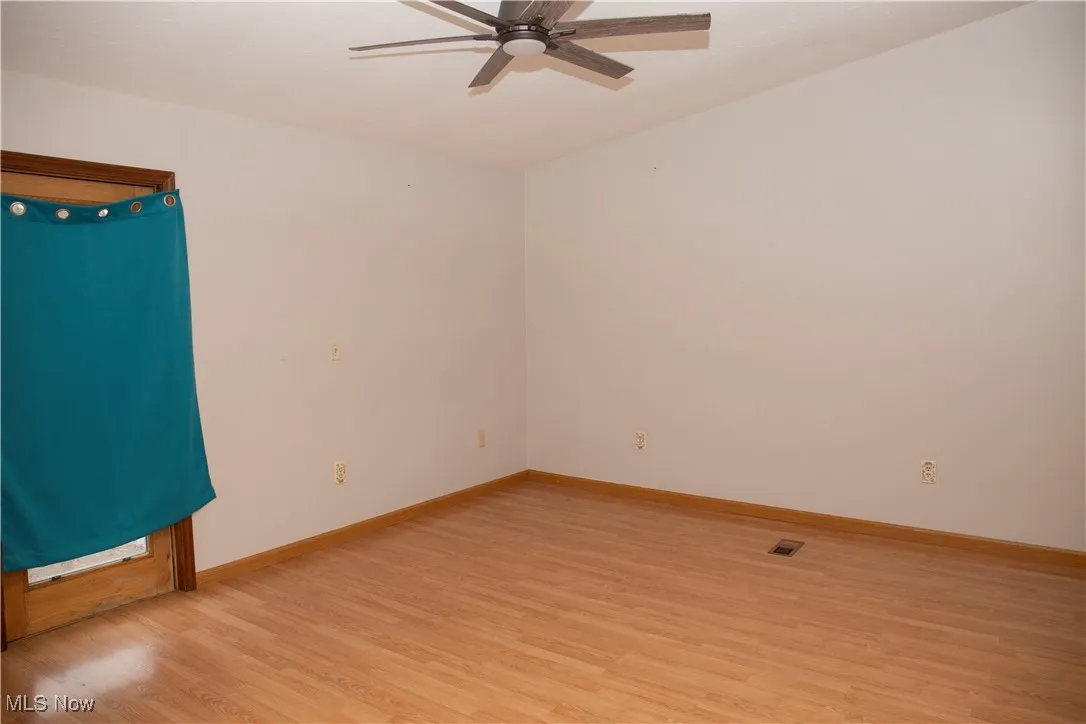 Spare room with a ceiling fan, visible vents, light wood finished floors, and baseboards