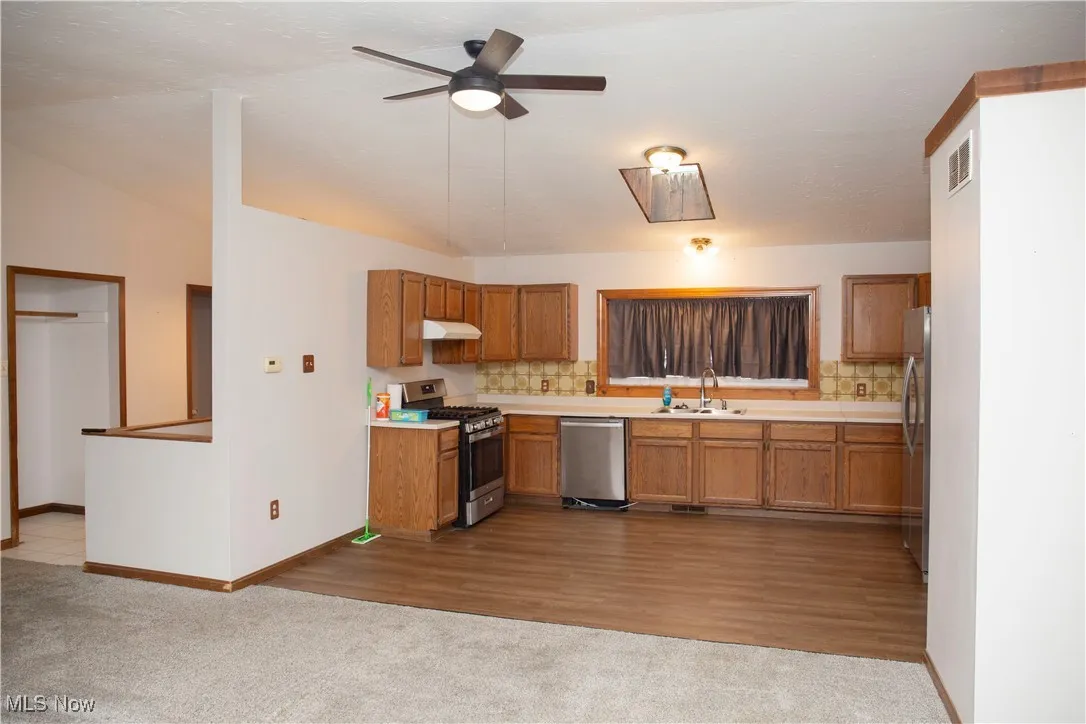 Kitchen featuring brown cabinetry, visible vents, a sink, under cabinet range hood, and appliances with stainless steel finishes