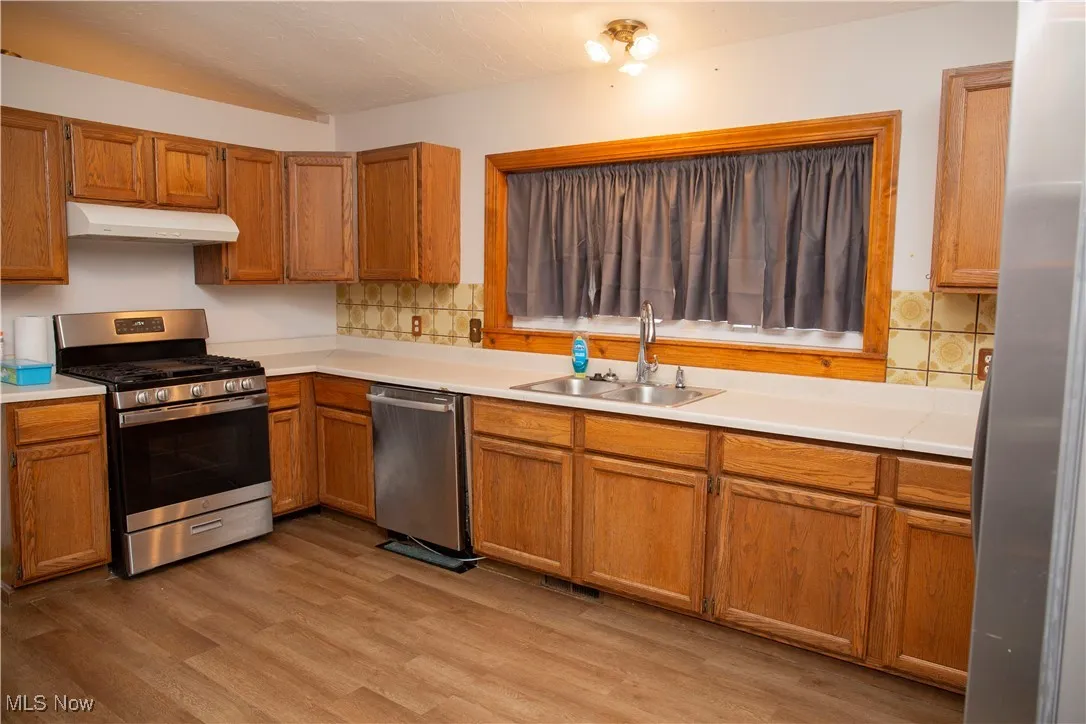 Kitchen with under cabinet range hood, a sink, stainless steel appliances, light wood finished floors, and light countertops
