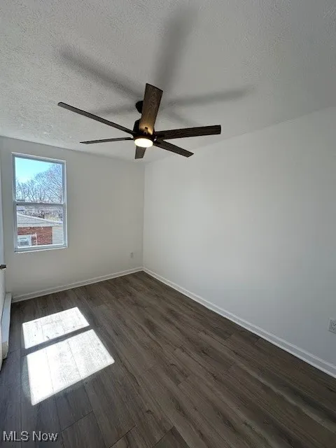 Empty room with a textured ceiling, baseboards, dark wood-type flooring, and a ceiling fan