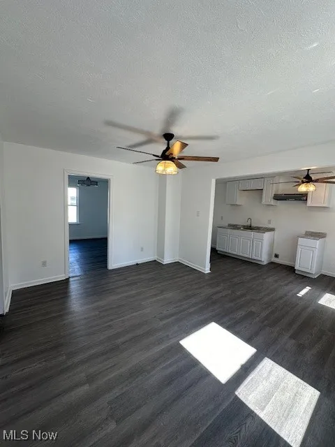 Unfurnished living room with dark wood finished floors, a sink, baseboards, and ceiling fan