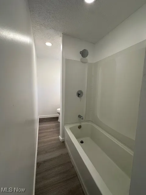 Bathroom featuring baseboards, toilet, bathtub / shower combination, wood finished floors, and a textured ceiling