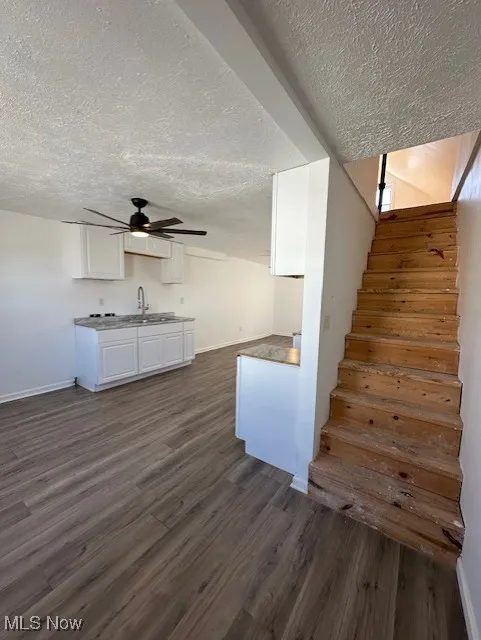 Stairs with ceiling fan, wood finished floors, baseboards, and a textured ceiling