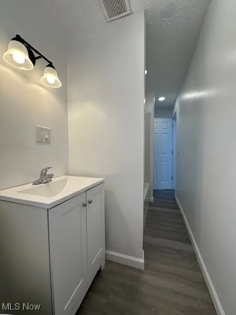 Bathroom with visible vents, a textured ceiling, wood finished floors, baseboards, and vanity