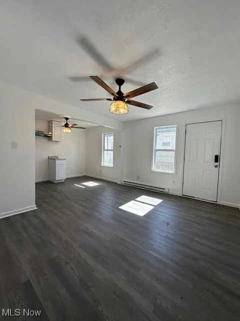 Unfurnished living room with ceiling fan, a baseboard radiator, baseboards, and dark wood finished floors