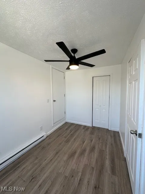 Unfurnished bedroom featuring a textured ceiling, wood finished floors, a closet, baseboards, and baseboard heating