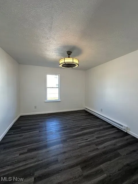 Spare room with a baseboard heating unit, baseboards, a textured ceiling, and dark wood-style floors