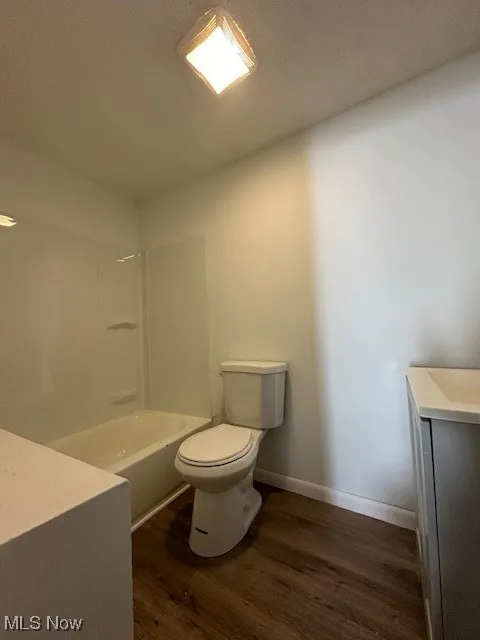 Bathroom featuring vanity, washtub / shower combination, wood finished floors, baseboards, and toilet