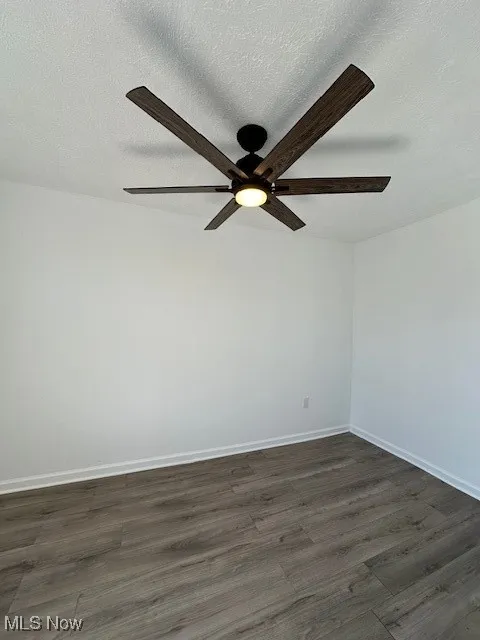 Spare room with dark wood finished floors, a ceiling fan, baseboards, and a textured ceiling