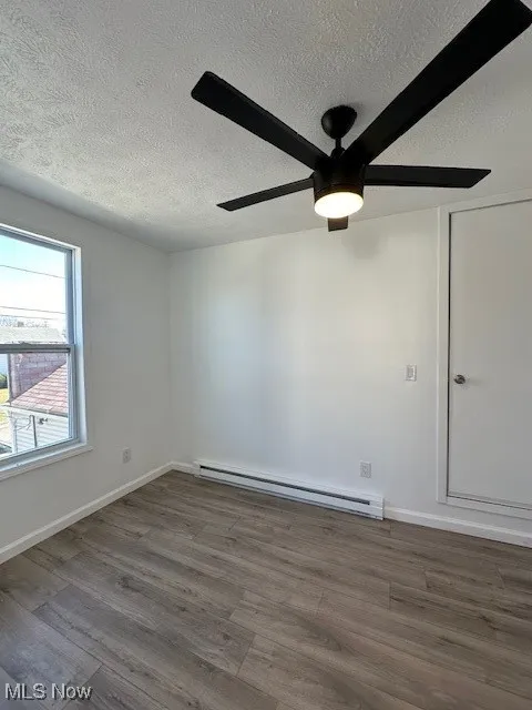 Spare room featuring a baseboard heating unit, baseboards, wood finished floors, a textured ceiling, and a ceiling fan