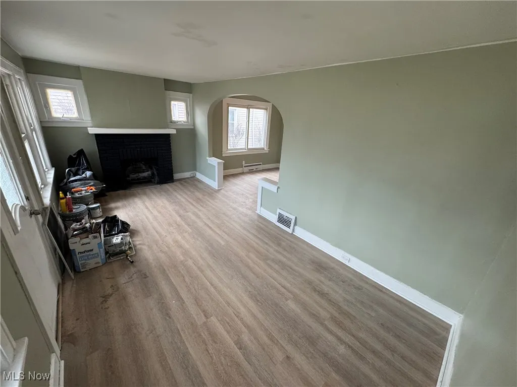 Unfurnished living room featuring wood finished floors, visible vents, baseboards, arched walkways, and a brick fireplace