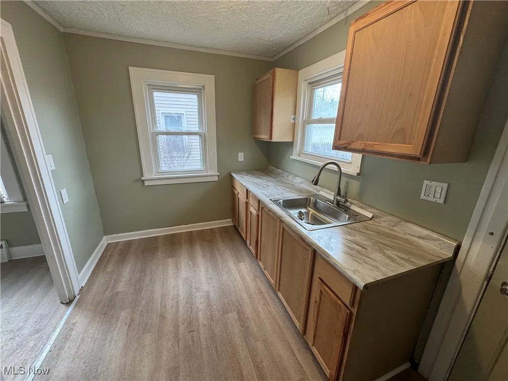 Kitchen featuring baseboards, a sink, light countertops, a textured ceiling, and light wood-type flooring