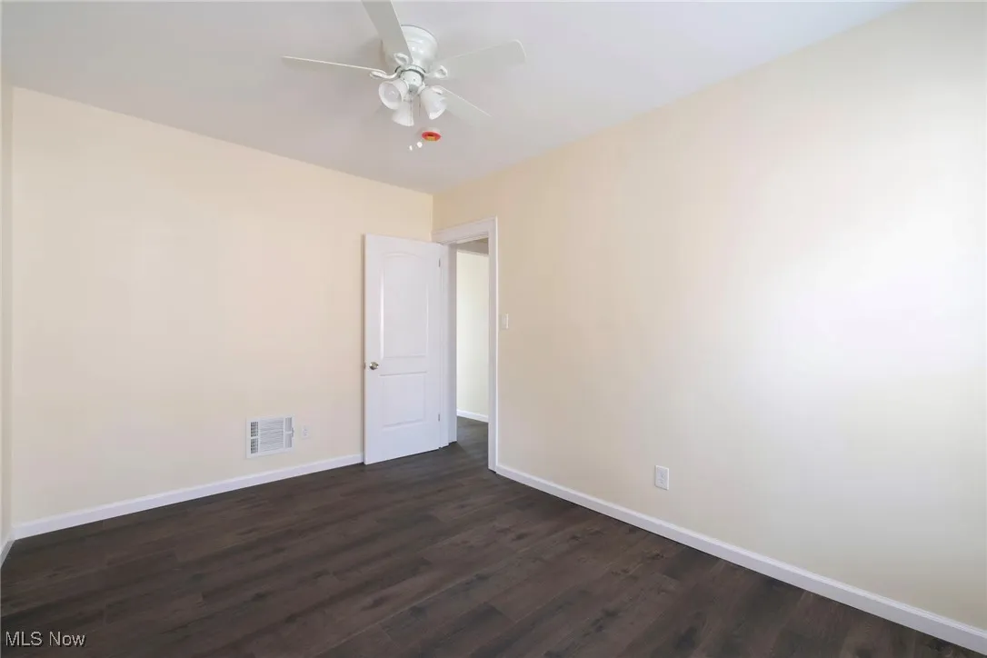 Spare room featuring visible vents, a ceiling fan, baseboards, and dark wood-style flooring