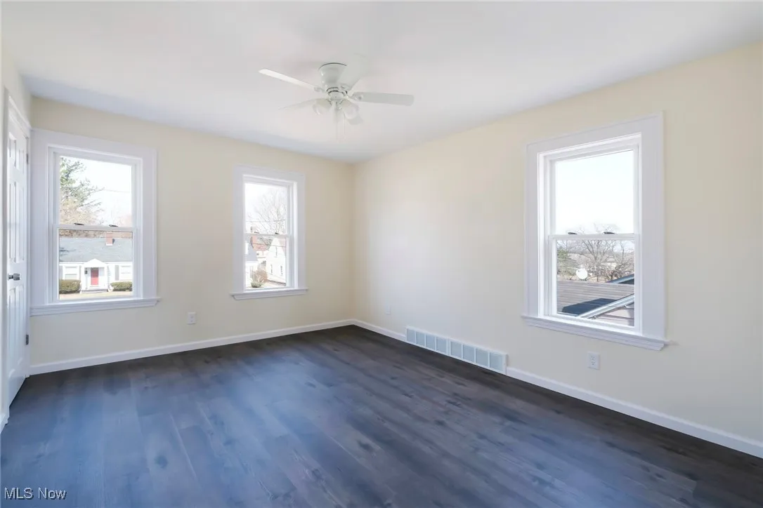 Unfurnished room with visible vents, a ceiling fan, dark wood-type flooring, and baseboards