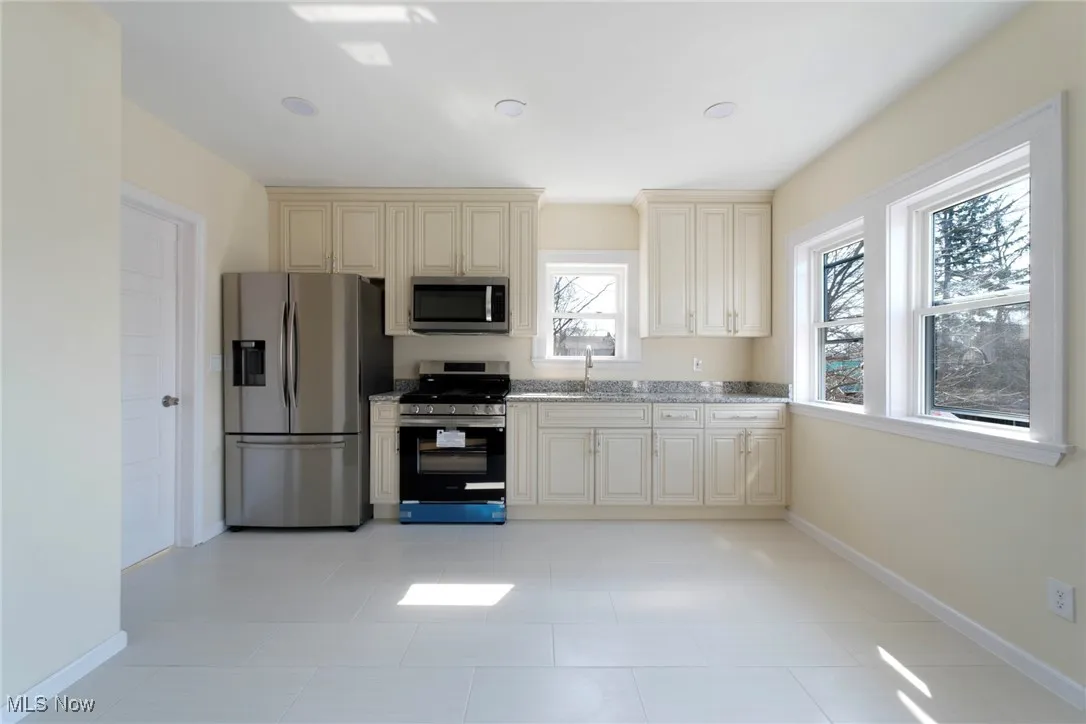 Kitchen featuring cream cabinetry, appliances with stainless steel finishes, baseboards, and a sink
