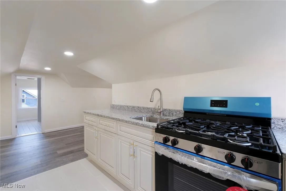 Kitchen with gas stove, light stone countertops, light wood-style flooring, a sink, and vaulted ceiling