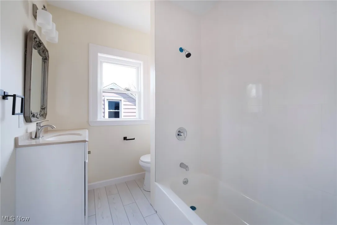Bathroom with baseboards, toilet, bathing tub / shower combination, wood finished floors, and vanity