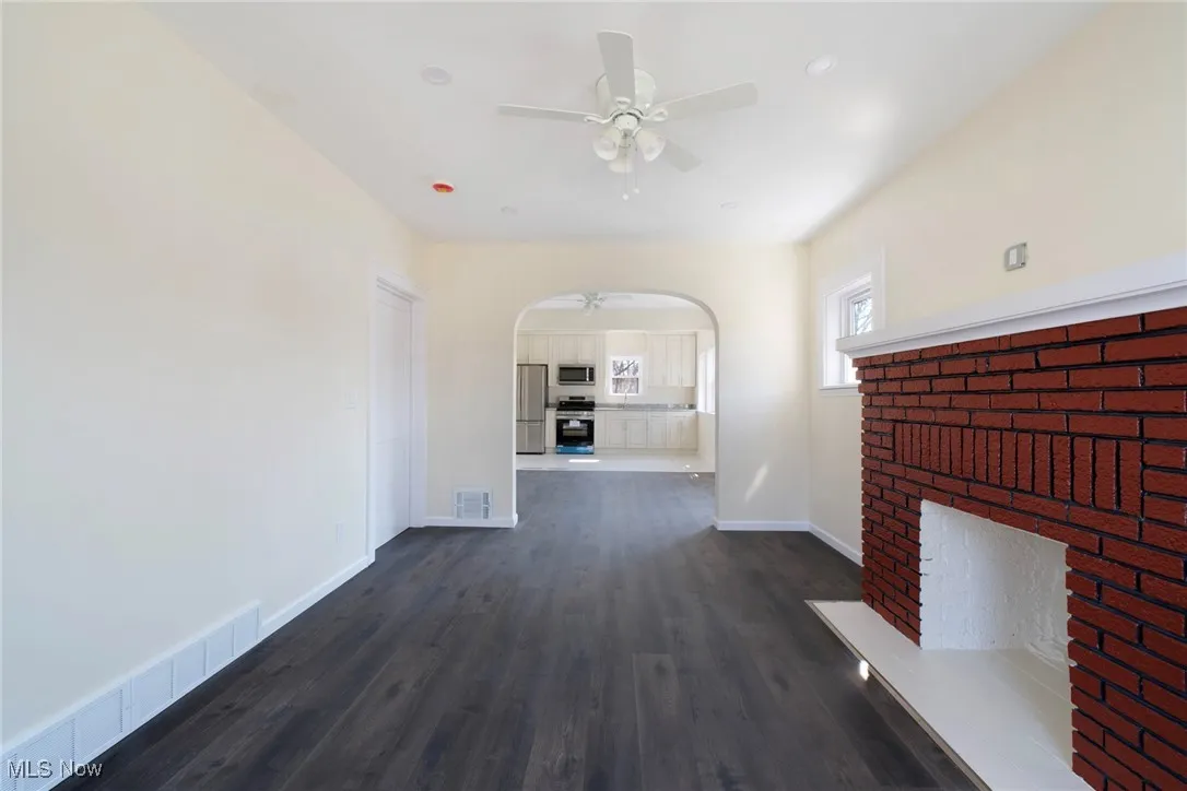 Unfurnished living room with arched walkways, visible vents, a fireplace, and ceiling fan