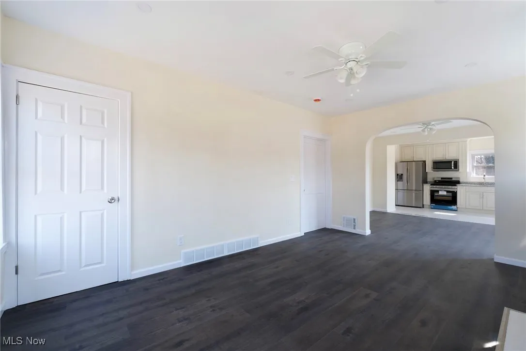 Unfurnished living room featuring dark wood finished floors, visible vents, a ceiling fan, and arched walkways