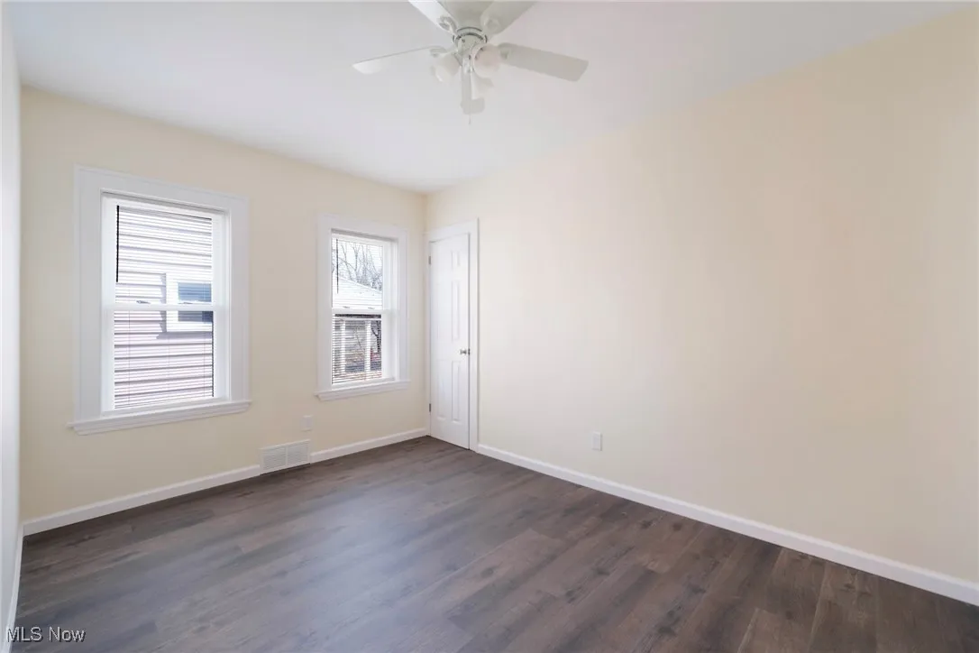 Unfurnished room with dark wood-style floors, baseboards, visible vents, and ceiling fan