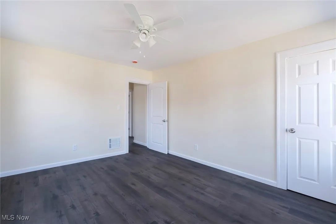 Unfurnished room with dark wood-style floors, visible vents, baseboards, and ceiling fan