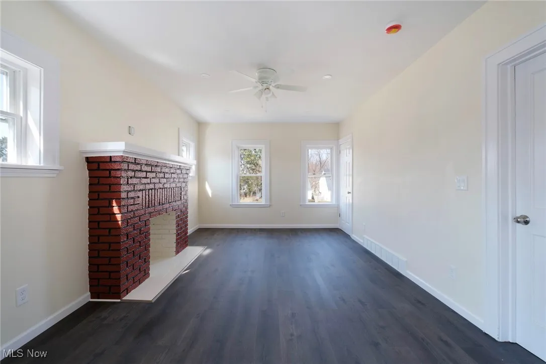 Unfurnished living room featuring baseboards, visible vents, a fireplace, ceiling fan, and dark wood-type flooring