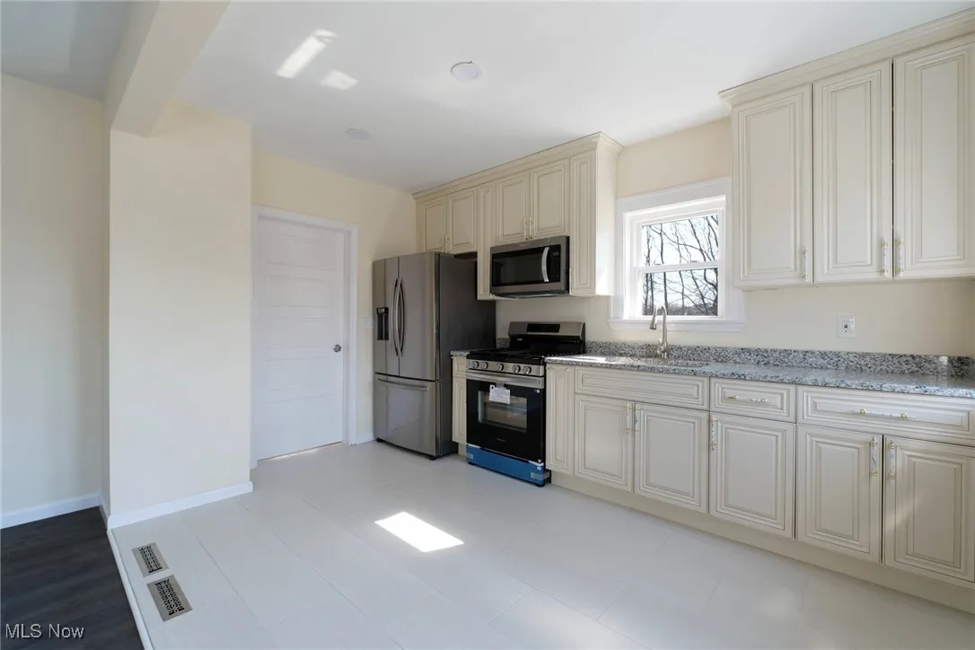 Kitchen featuring baseboards, light stone countertops, cream cabinetry, stainless steel appliances, and a sink